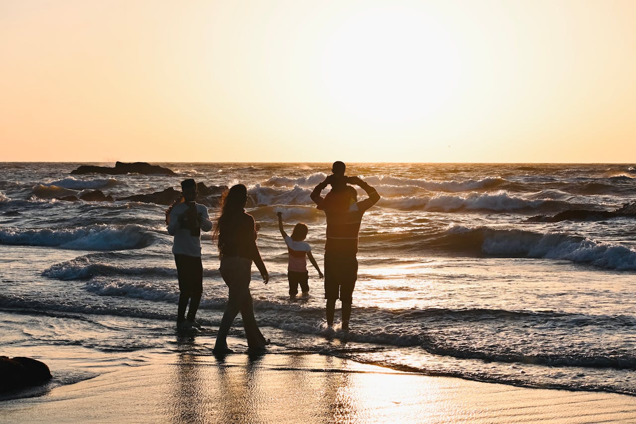 Silhouetted family enjoying a vibrant sunset at a beach in Goa, India.